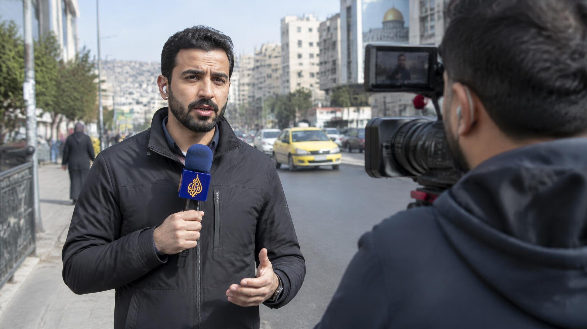 Reporter holding a microphone recording a piece to camera outdoors